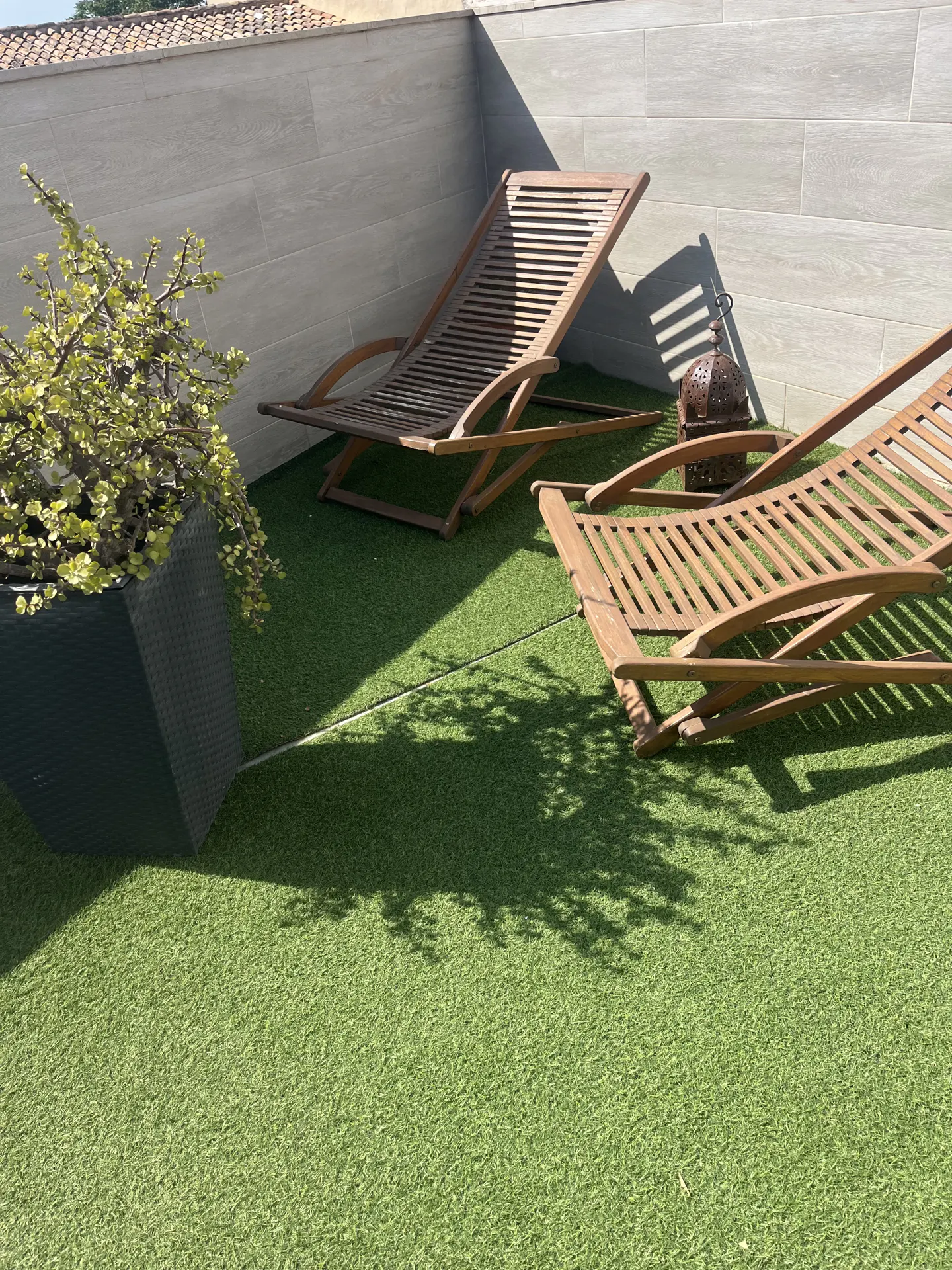 Outdoor patio with two wooden lounge chairs on green turf, a potted plant, and a decorative lantern.