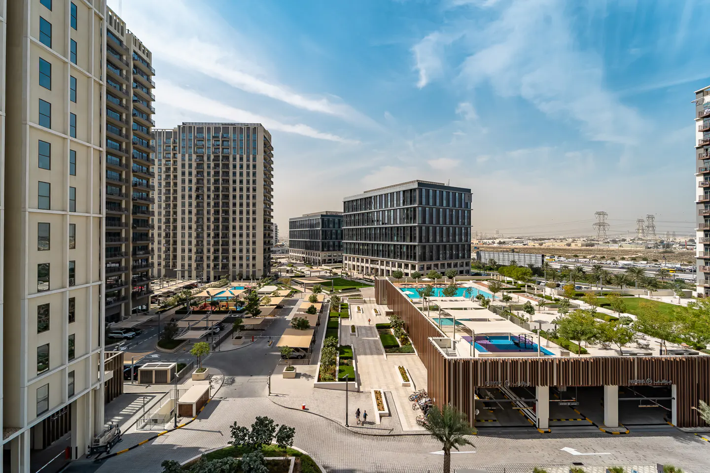 High-angle view of a modern apartment complex with swimming pools, landscaped courtyards, and parking under a blue sky.