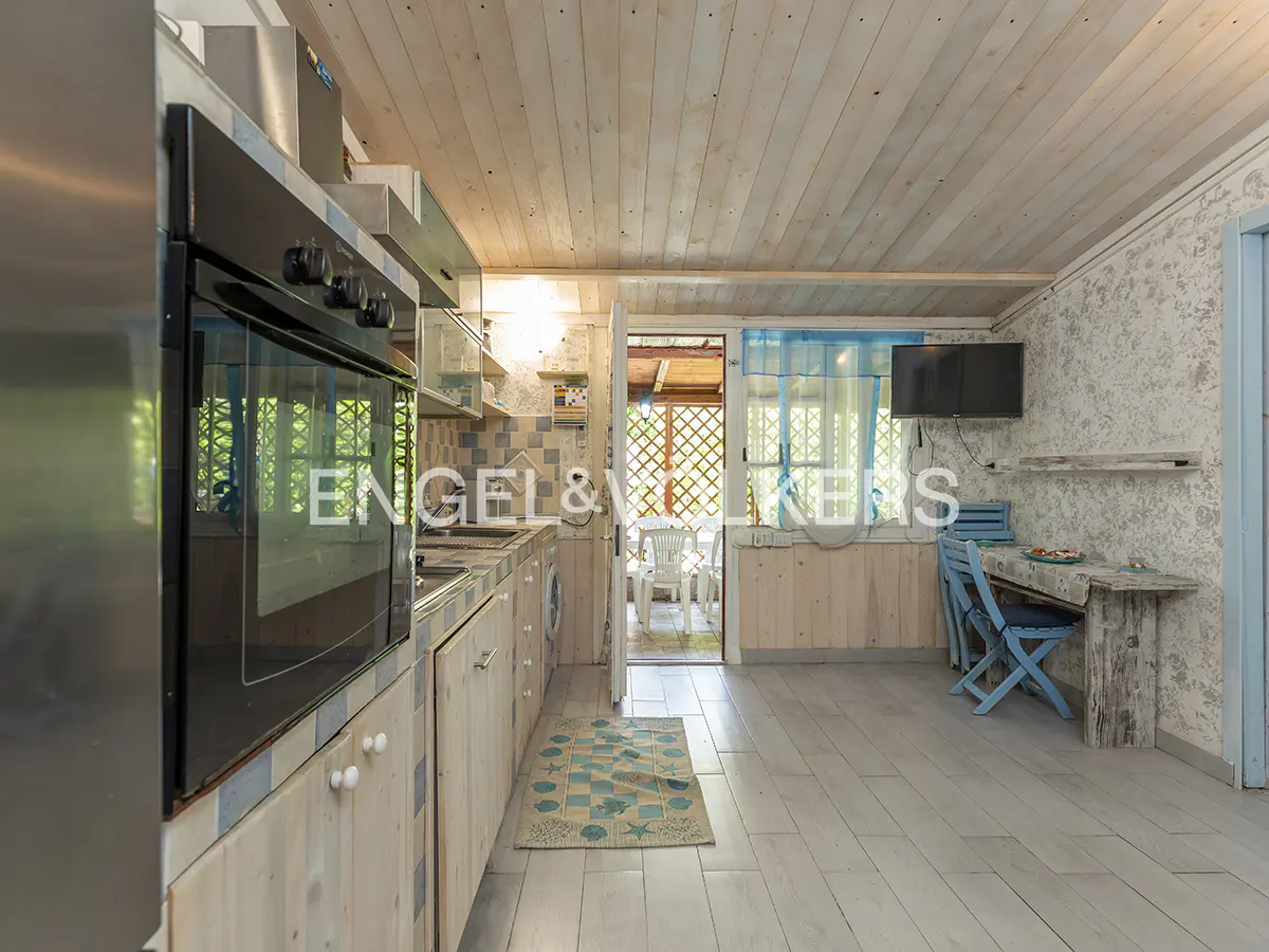 A bright kitchen with white wood cabinets, a black oven, and a blue table and chairs. An open door leads to an outdoor patio.