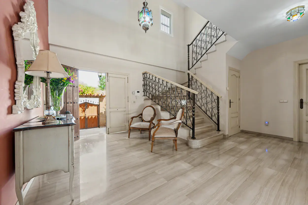 Elegant foyer with marble floors, a grand staircase with wrought iron railings, two armchairs, and a decorative console.