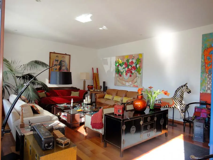 Bright living room with hardwood floors, white walls, and eclectic decor. Sofas, art, a zebra statue, and a black cabinet are visible.