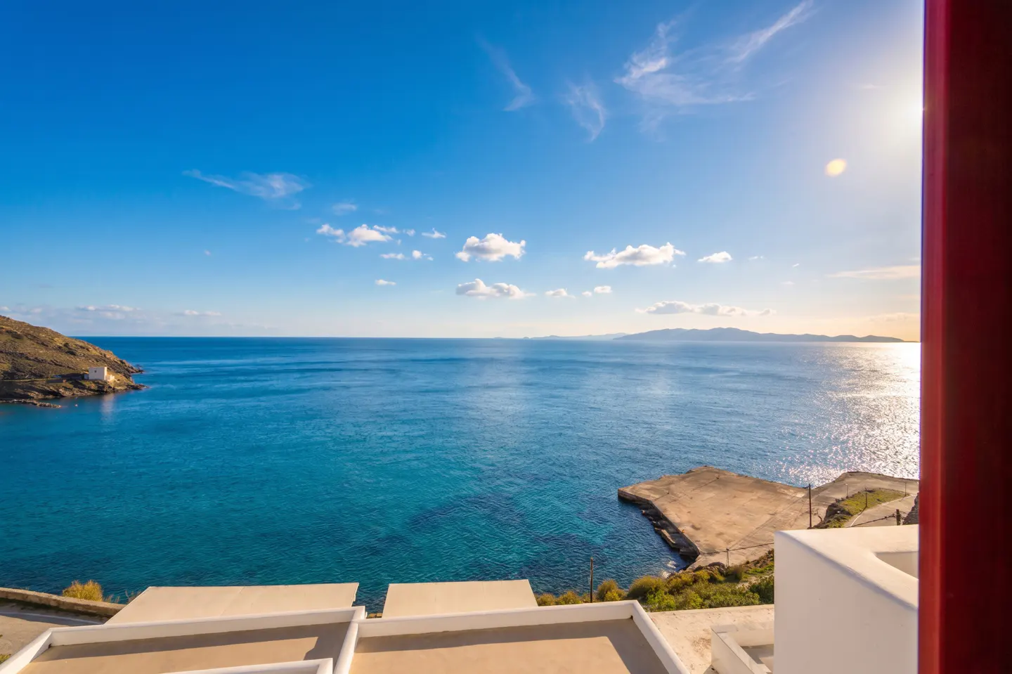 Ocean view from a white building with a red frame. Blue sea and sky with a small island and dock visible.