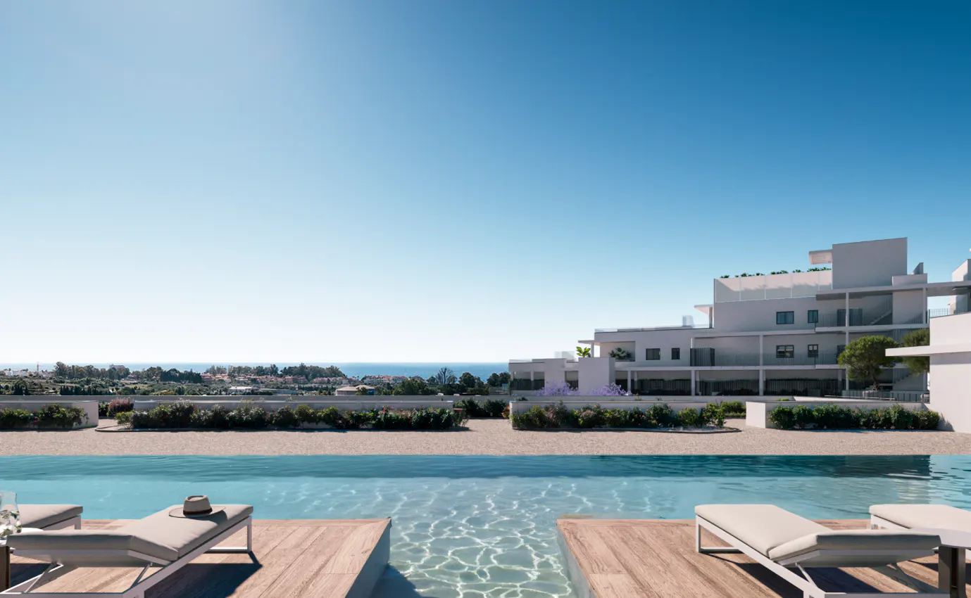 Luxury condo view with pool, lounge chairs, and ocean backdrop under a clear blue sky. Modern white building in the background.