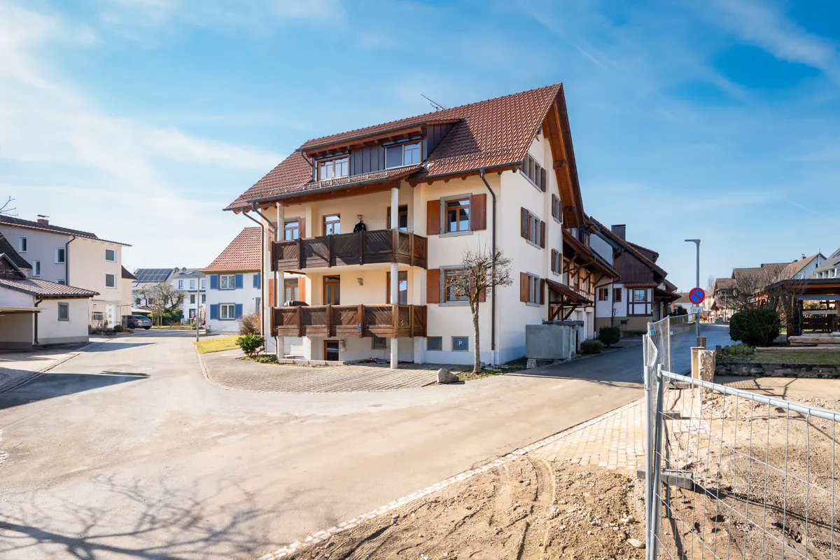 Exterior view of a two-story house with brown shutters and balconies on a sunny day.