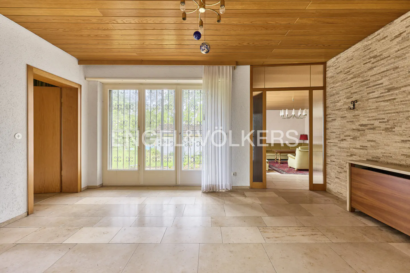 A bright, empty room with a wood ceiling, stone floors, and a wall of windows.