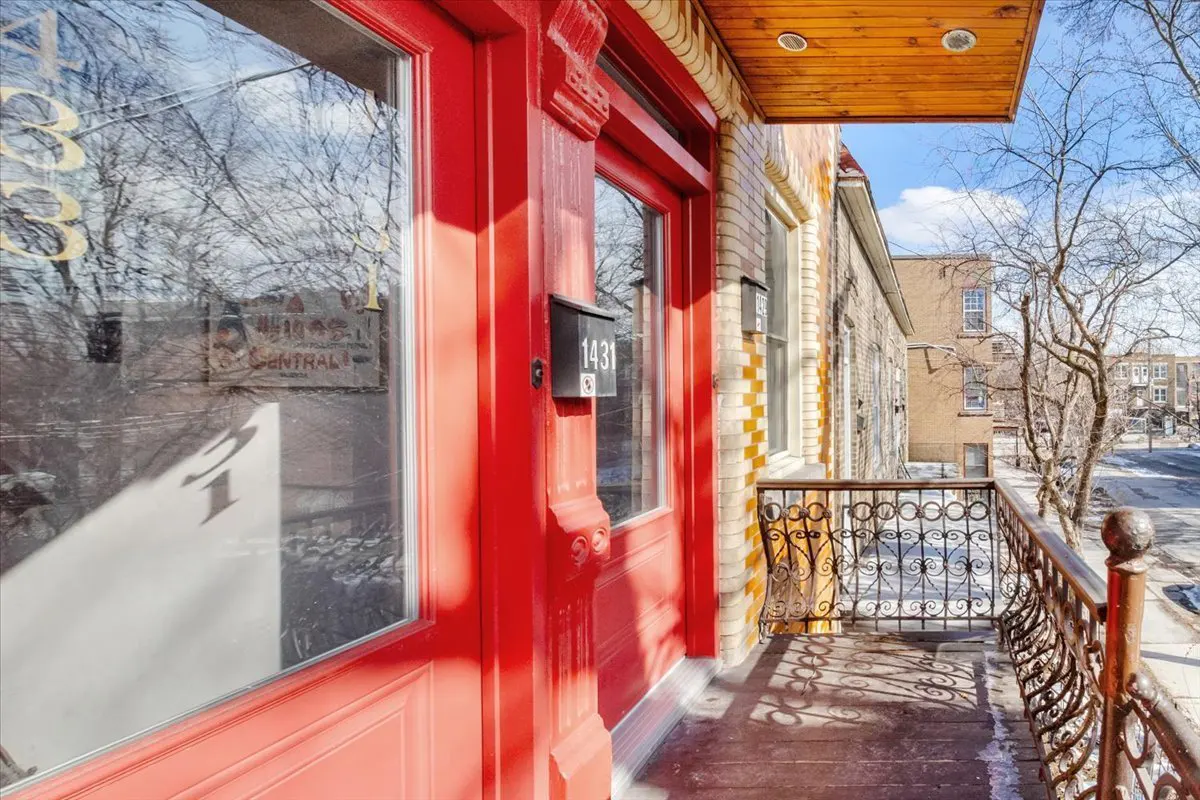 Exterior view of a building with a red door, black mailbox with the number 1431, and a wrought iron balcony.