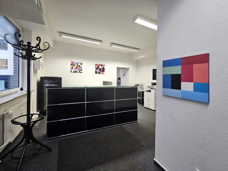 Office reception area with a black desk, coat rack, and colorful geometric art on the white walls.