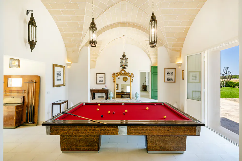 Bright game room with a red pool table, hanging lanterns, and arched stone ceiling.
