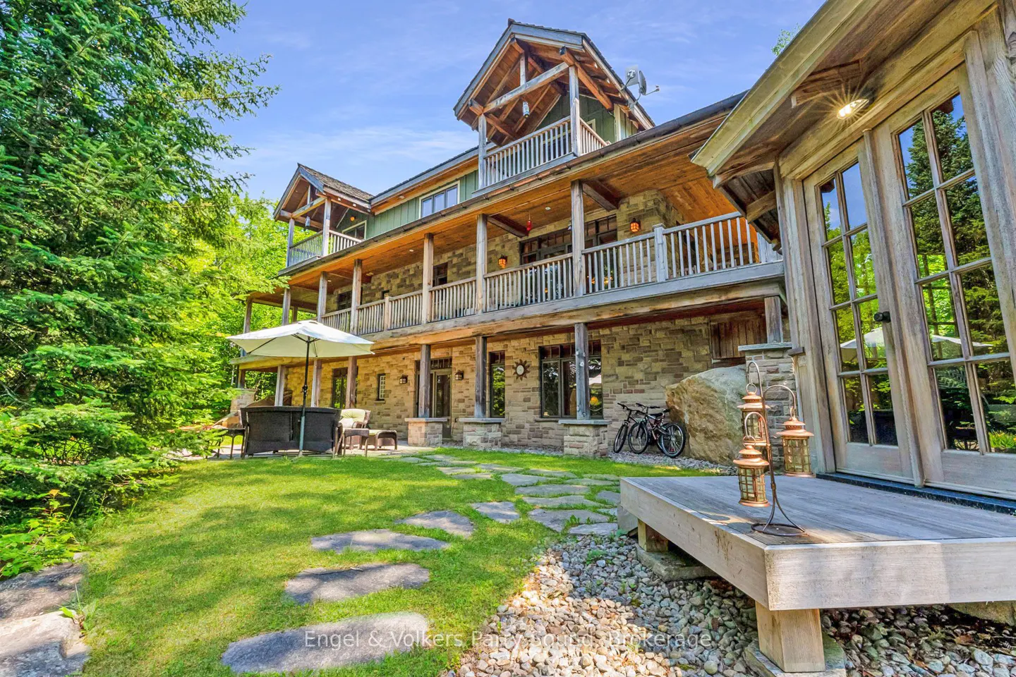 Exterior view of a multi-story stone house with wooden balconies, a green lawn, and a stone pathway.