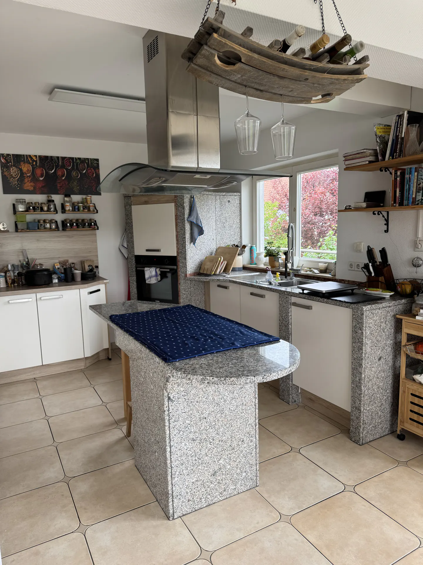 Bright kitchen with white cabinets, granite countertops, and a blue patterned tablecloth on the island. A wine rack hangs above.