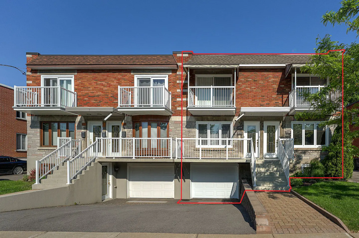 Two-story brick townhouse with white balconies and garage doors. Stairs lead to the front doors. A tree is on the right.