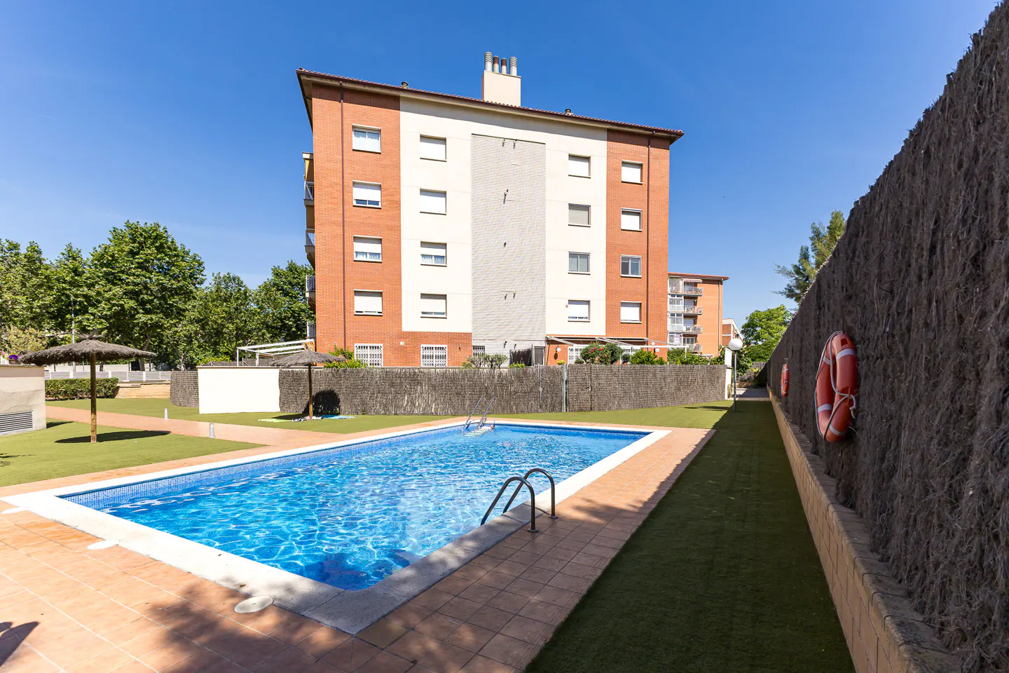 Apartment complex with a blue swimming pool, brown tile, and a tall fence with orange life preservers.