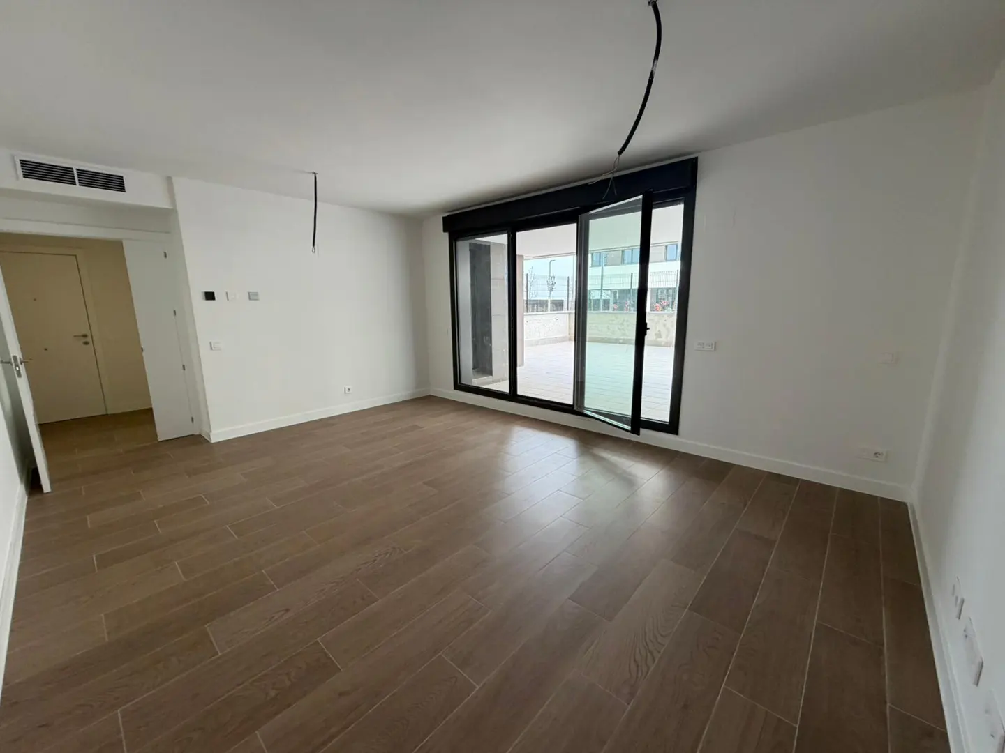 An empty room with wood floors, white walls, and a large sliding glass door to a balcony.