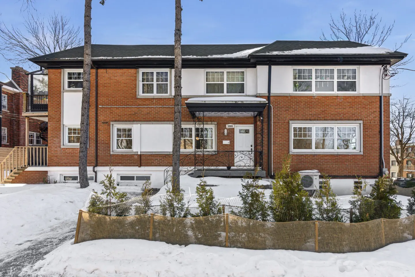 Two-story brick house with white trim, black roof, and snow-covered yard. A black awning covers the white front door.