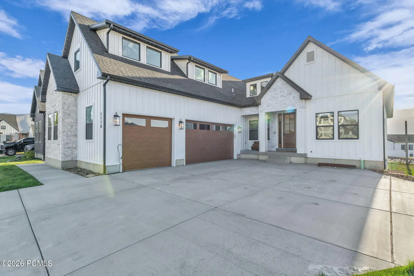 Two-story white farmhouse with a gray roof, brown garage doors, and a large concrete driveway under a blue sky.
