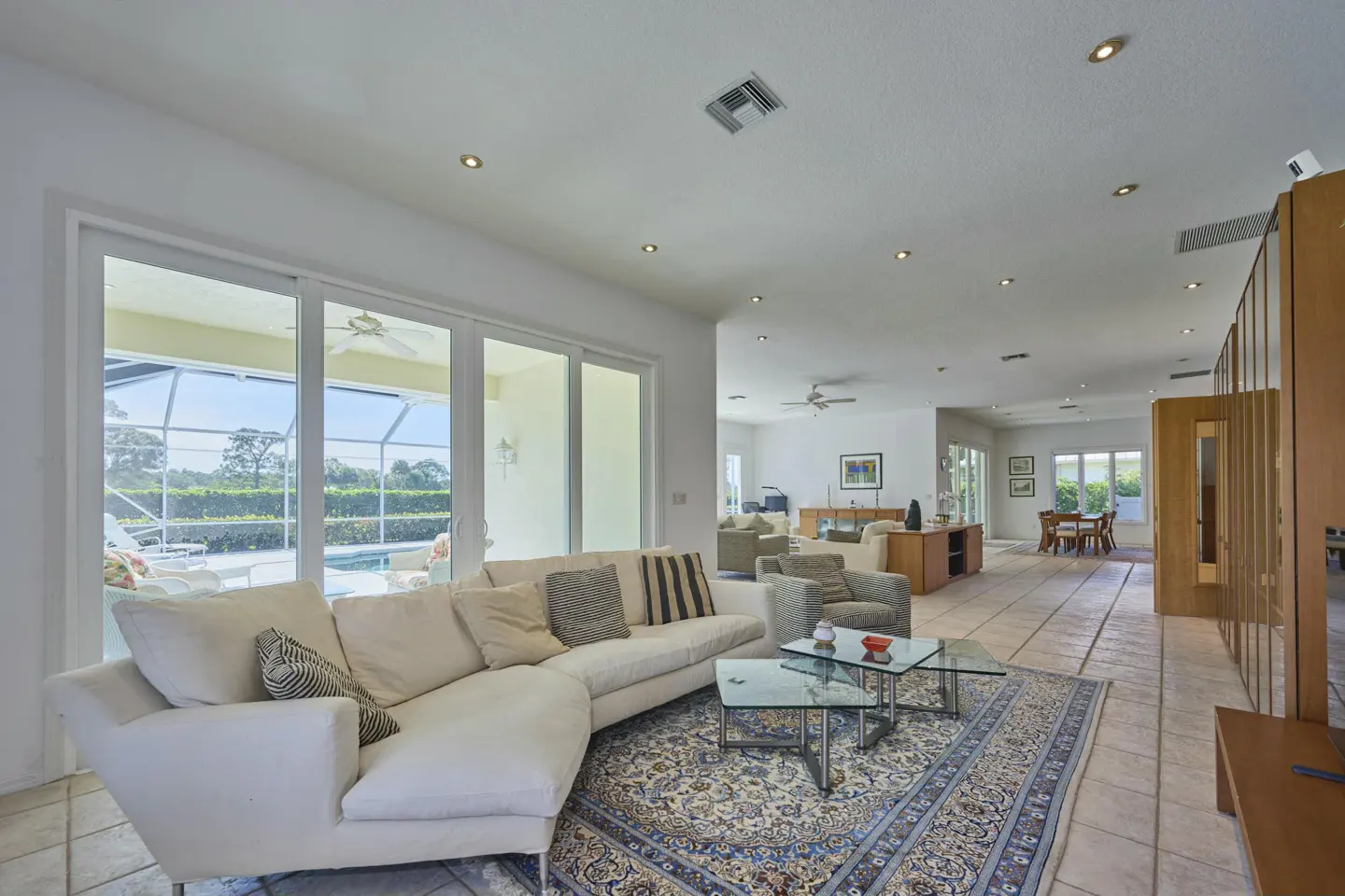 Bright living room with white sectional sofa, glass tables on a patterned rug, and sliding glass doors to a screened pool area.