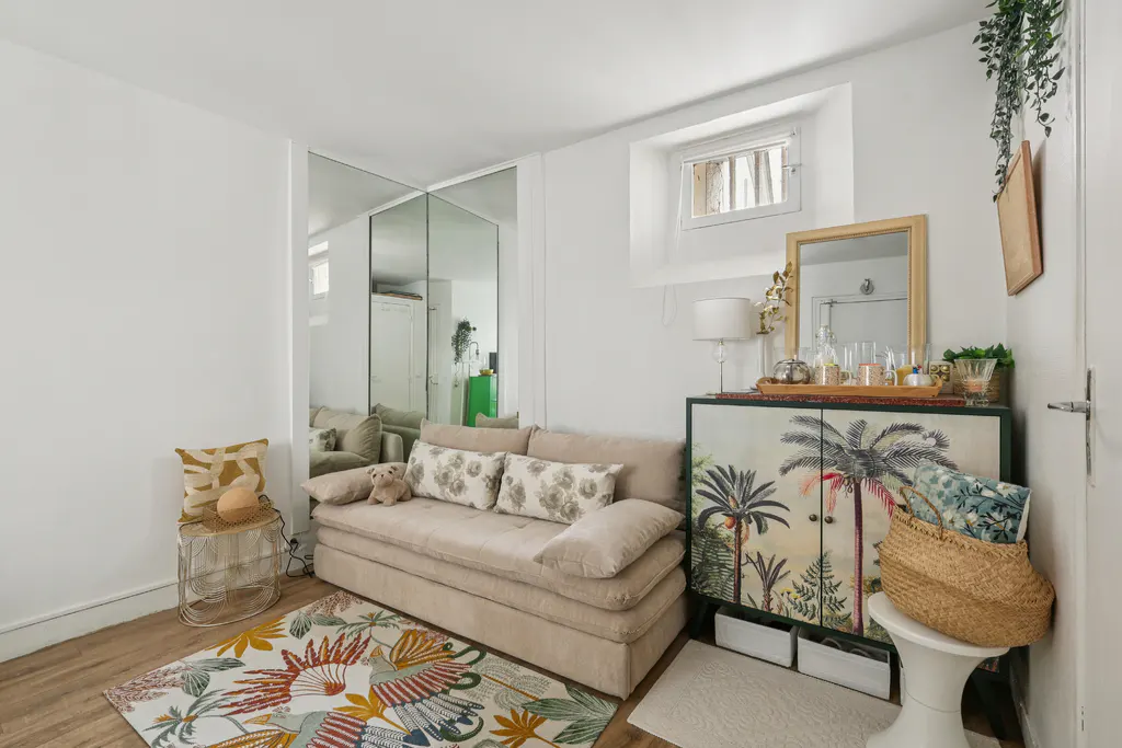 Cozy living room with a beige sofa, floral rug, and a cabinet with a palm tree design. A mirror reflects the room, enhancing the sense of space.