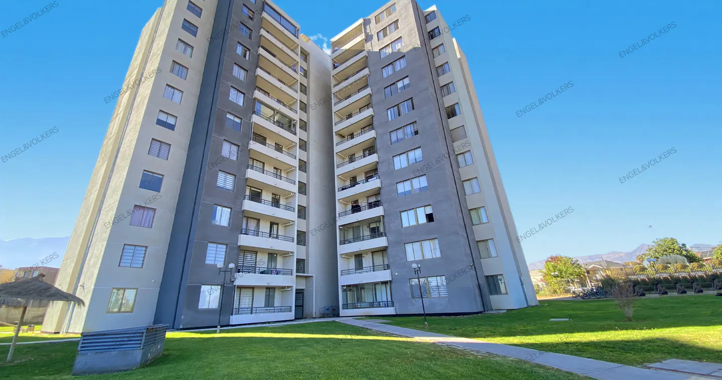 Exterior view of a tall, gray apartment building with balconies, green lawn, and blue sky.