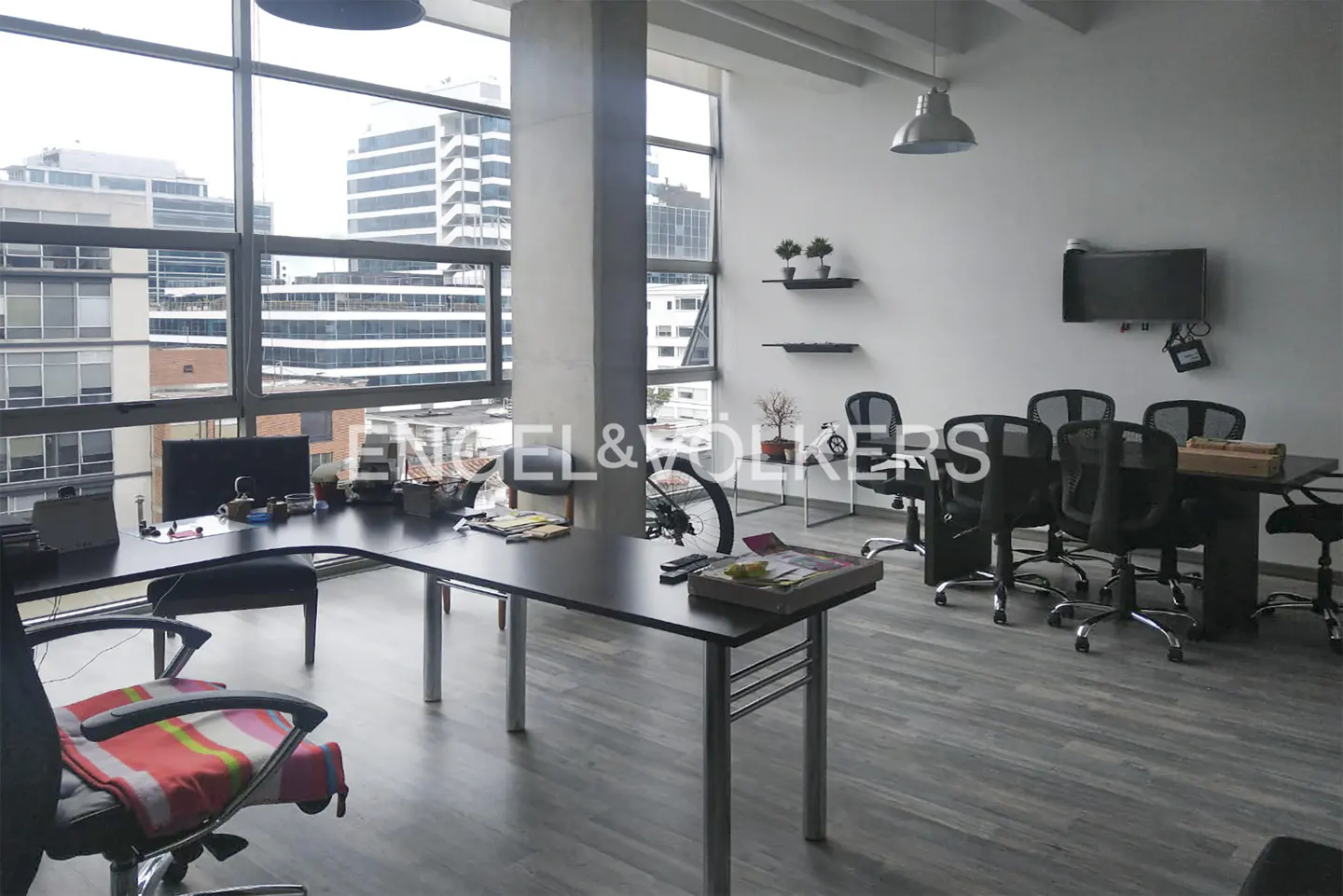 Bright office space with large windows, black desks, and rolling chairs. A bicycle is parked near a small table with plants.