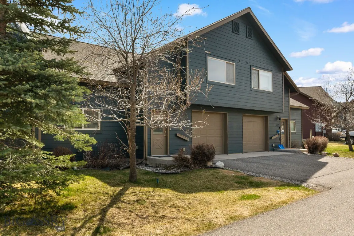Two-story townhouse with blue siding, two garage doors, and a small yard on a sunny day.