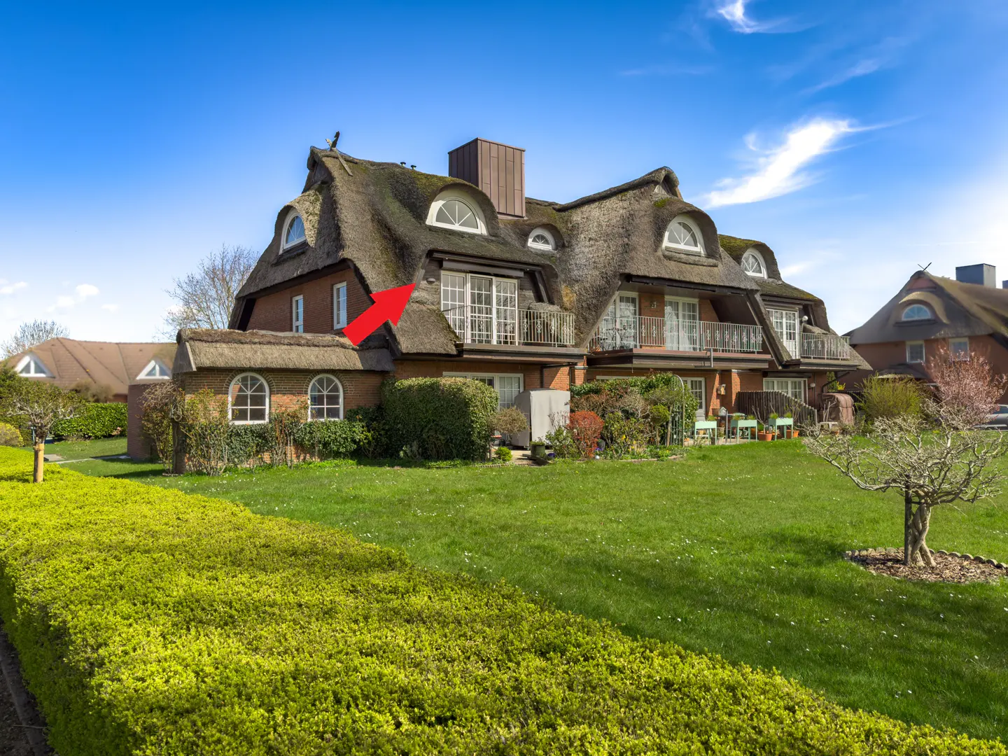 A multi-story house with a thatched roof, balconies, and a green lawn under a blue sky.