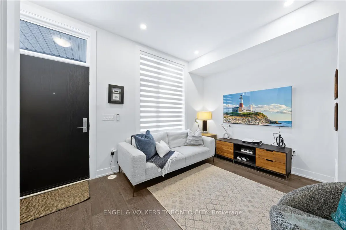 Bright living room with a black front door, white sofa with blue pillows, and a TV showing a lighthouse scene.