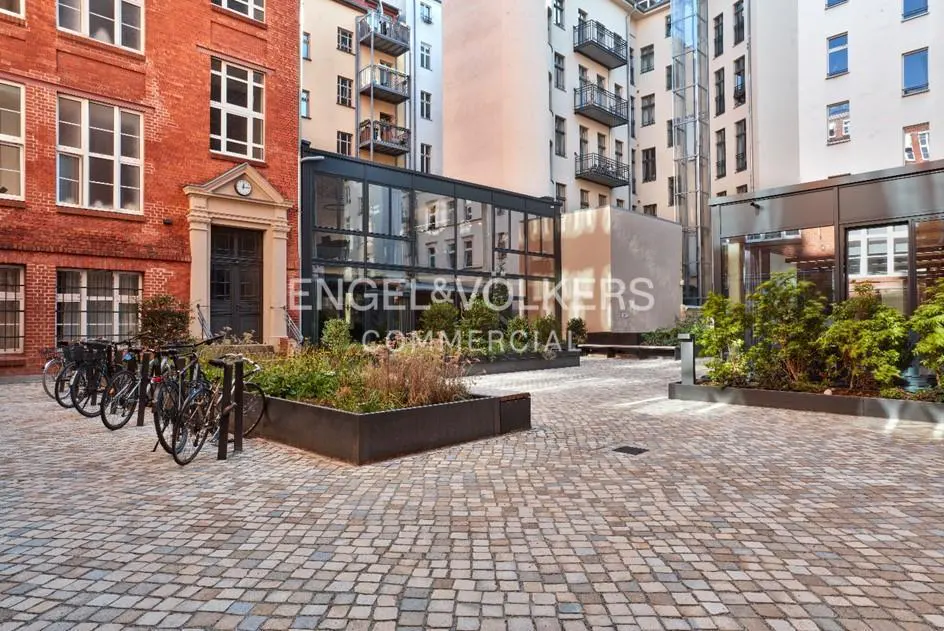 Courtyard view of a brick building with bikes parked outside, a glass building, and cobblestone ground.