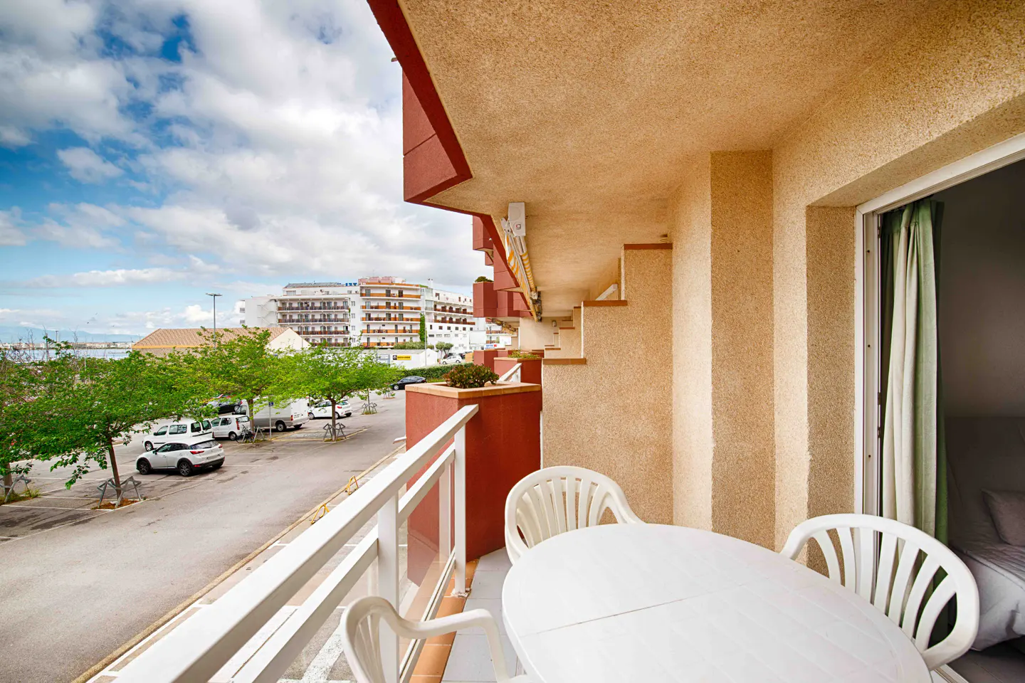 Balcony view with white table and chairs overlooking a parking lot, trees, and buildings under a cloudy sky.