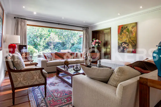 A bright living room with sofas, a patterned rug, and a large window overlooking a lush green garden.