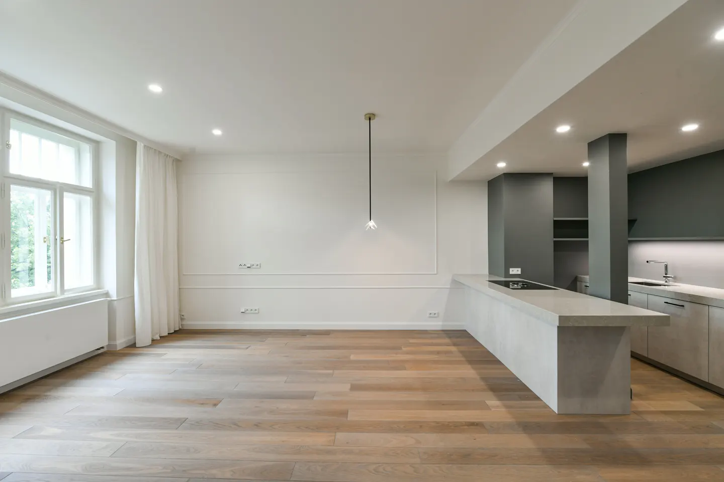 Bright, modern apartment with wood floors, white walls, and a gray kitchen island. A window with white curtains lets in natural light.