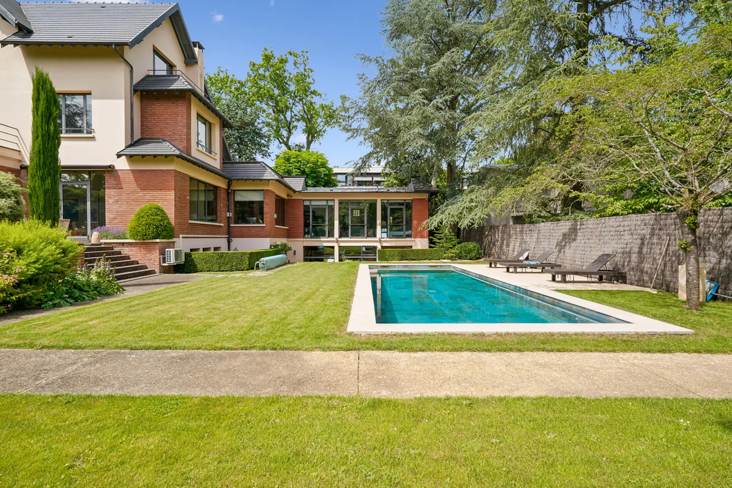 Backyard of a brick and stucco home featuring a rectangular swimming pool, manicured lawn, and lounge chairs.