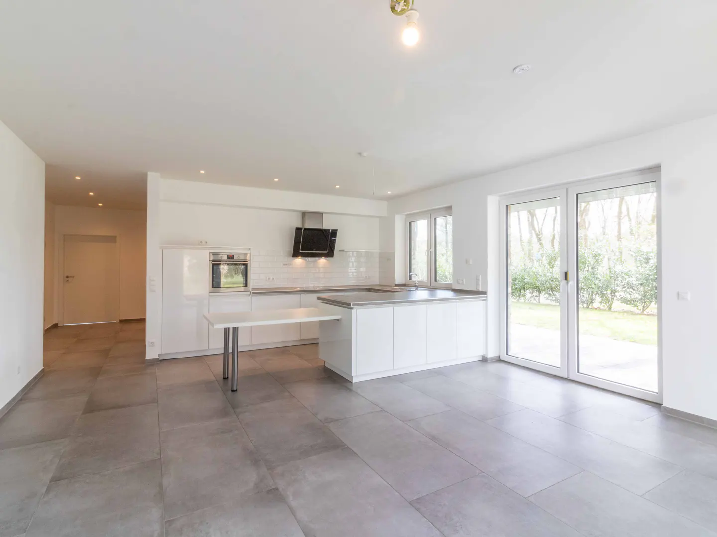 Bright, modern kitchen with white cabinets, stainless steel appliances, and gray tile floor. Sliding glass doors lead to a green backyard.