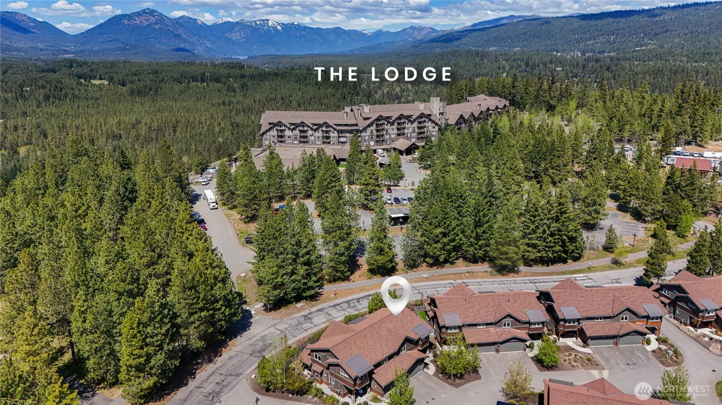 Aerial view of The Lodge, a large mountain resort surrounded by dense pine forests and snow-capped peaks in the distance.