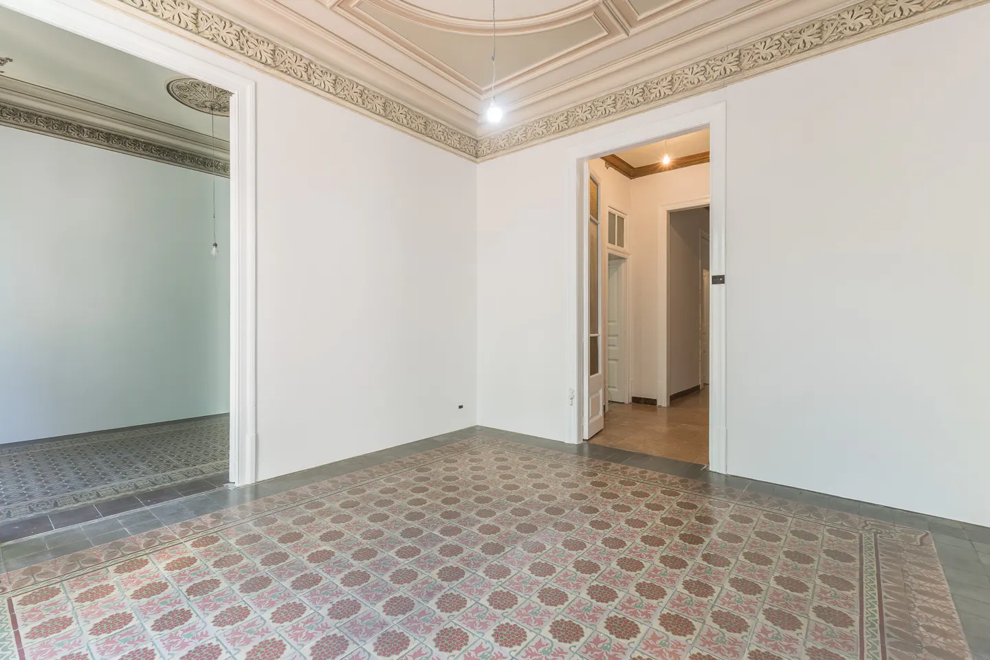 Empty room with white walls, decorative ceiling, and patterned tile floor. Doorways lead to other rooms.