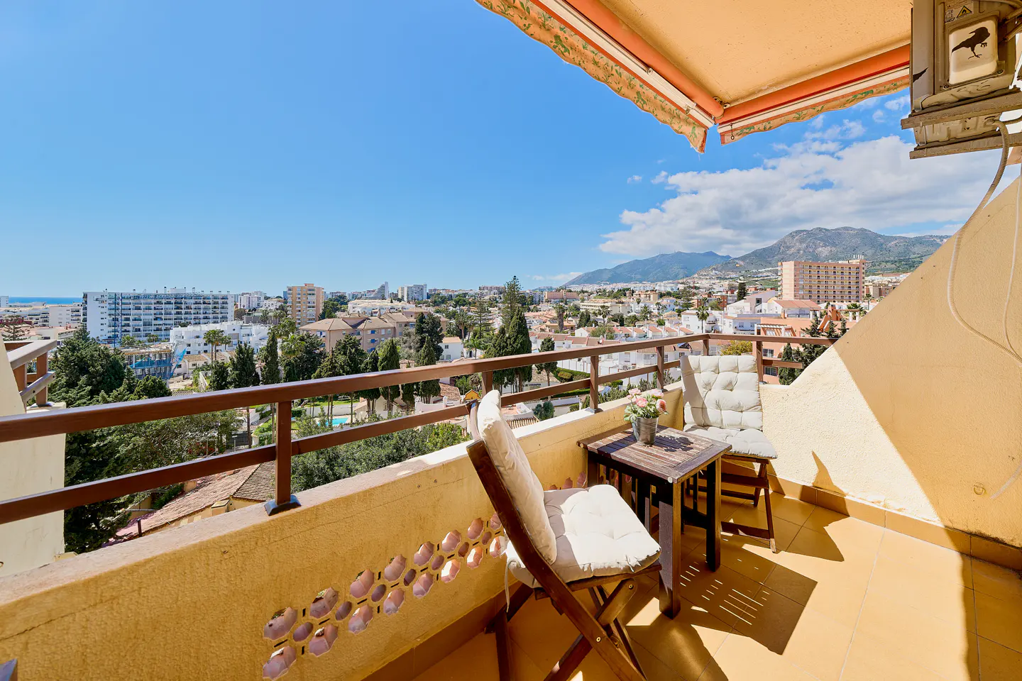 Balcony view with two chairs, a small table, and a city view under a blue sky.