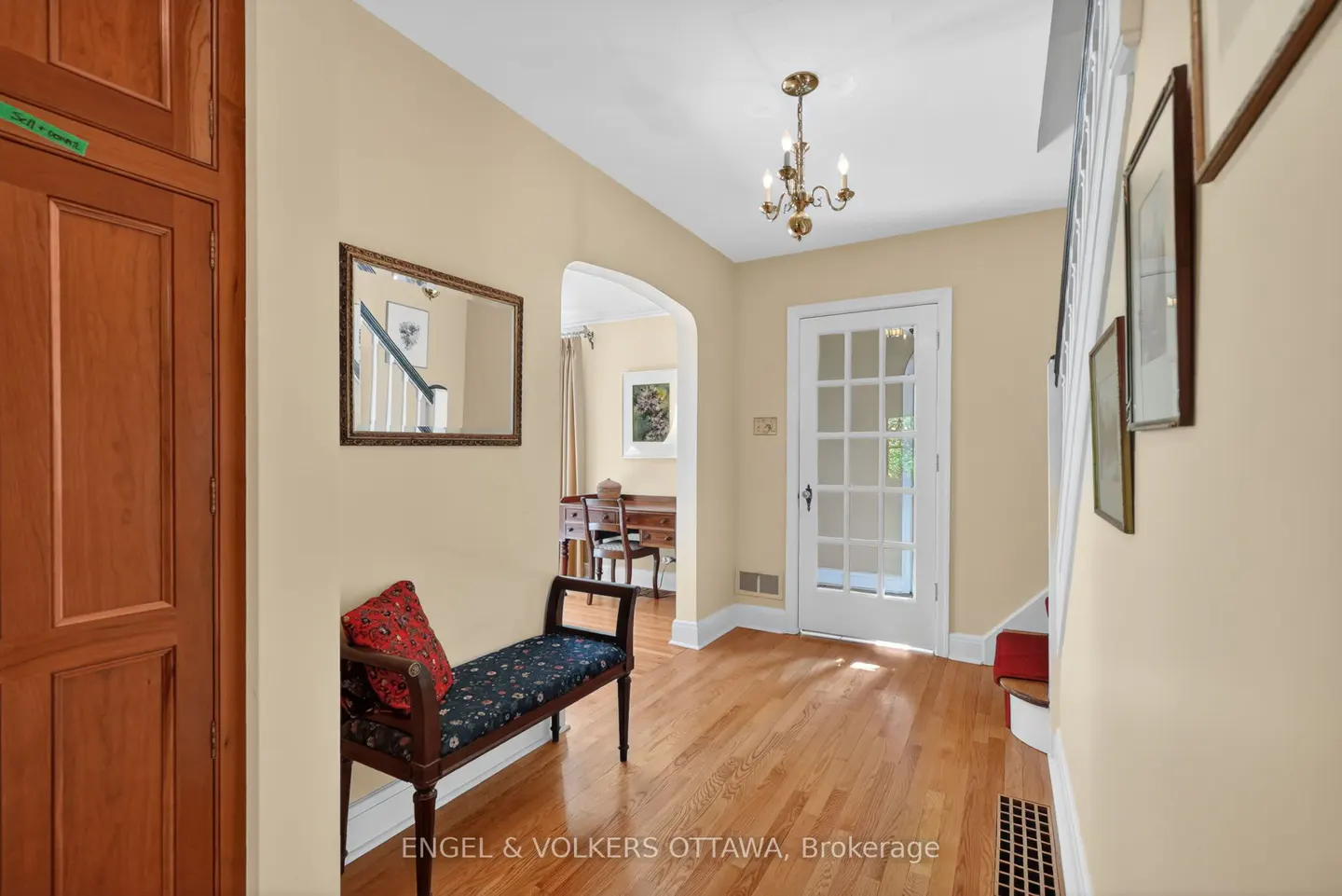 Foyer with wood floors, a bench with a red pillow, and a white door with glass panes. A mirror hangs on the wall.