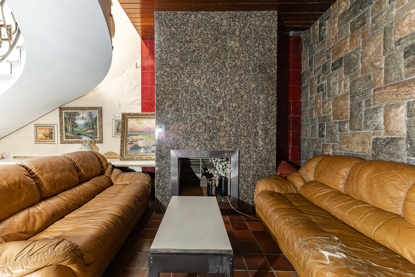 Living room with two tan leather sofas, a central coffee table, and a large granite fireplace against a stone wall.