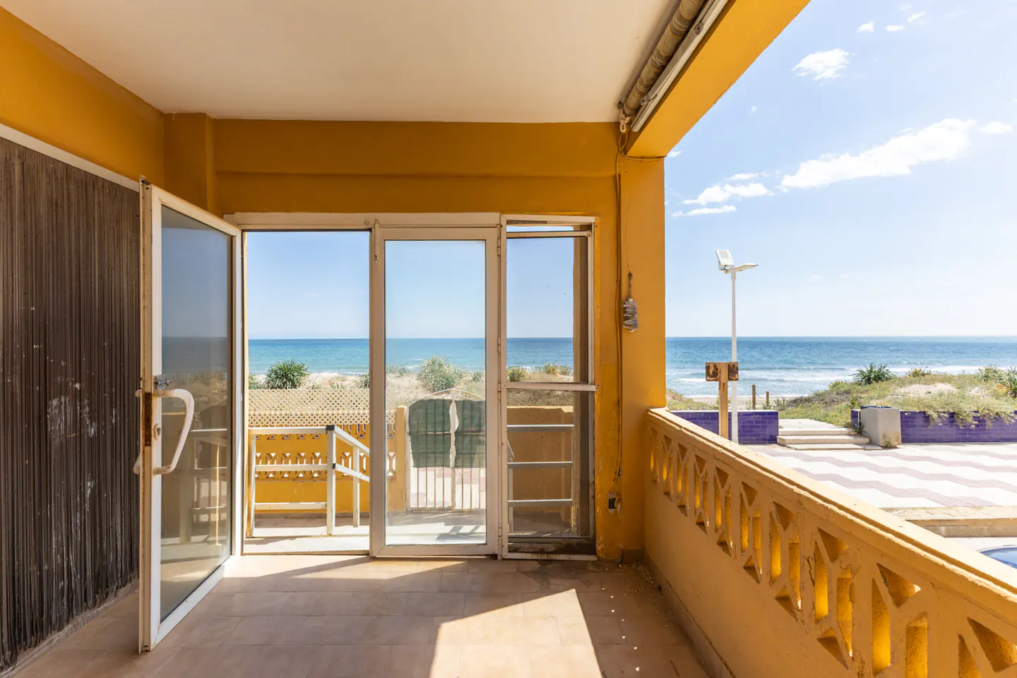 Balcony view of the ocean through open glass doors. Yellow walls and patterned railing. Blue sky and water visible.