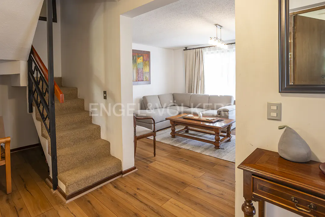 Interior view of a home featuring a carpeted staircase, wood floors, and a living room with a gray sofa and wooden coffee table.