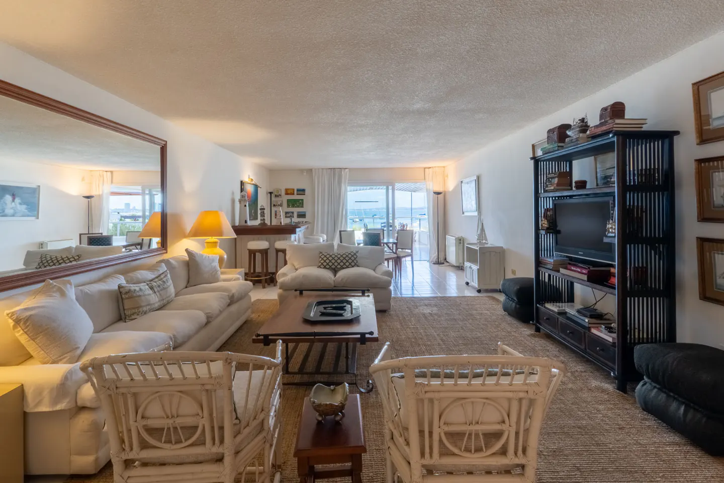 Bright living room with white sofas, two rattan chairs, a wooden coffee table, and a large black media unit facing the sea.