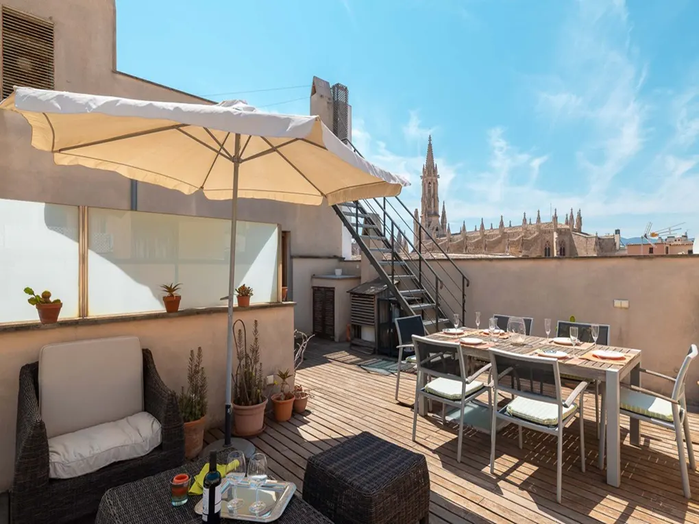 Rooftop patio with dining table set for six, lounge seating, and a view of a cathedral under a blue sky.