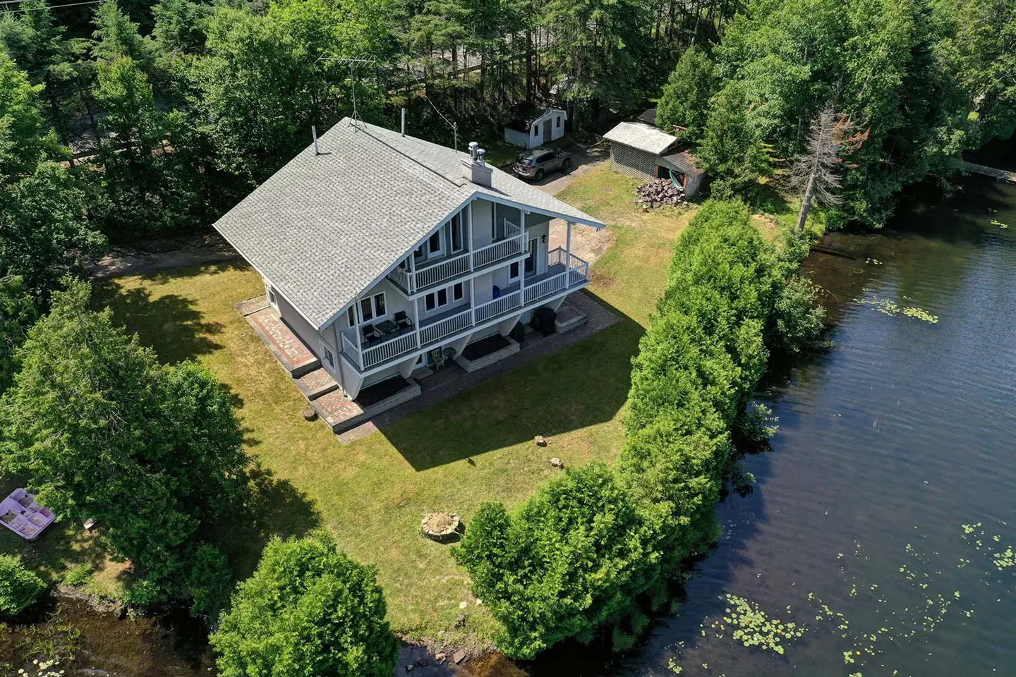 Aerial view of a two-story gray house with a gray roof, surrounded by green trees and a lake.