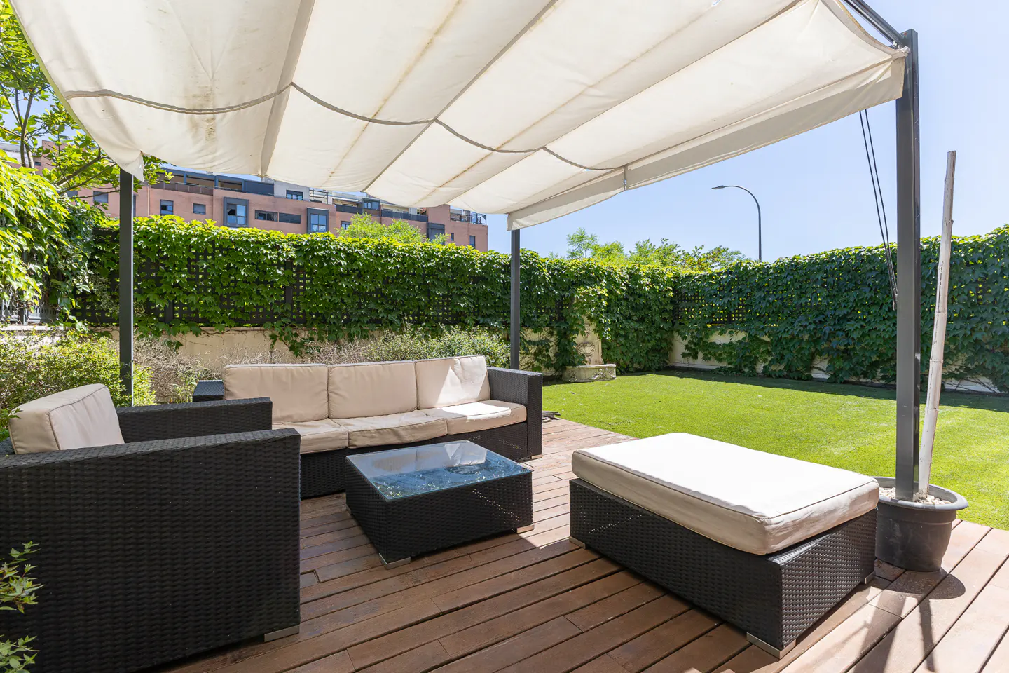 Outdoor patio with dark wicker sofa, chairs, and coffee table on a wooden deck under a white canopy, facing a green lawn.