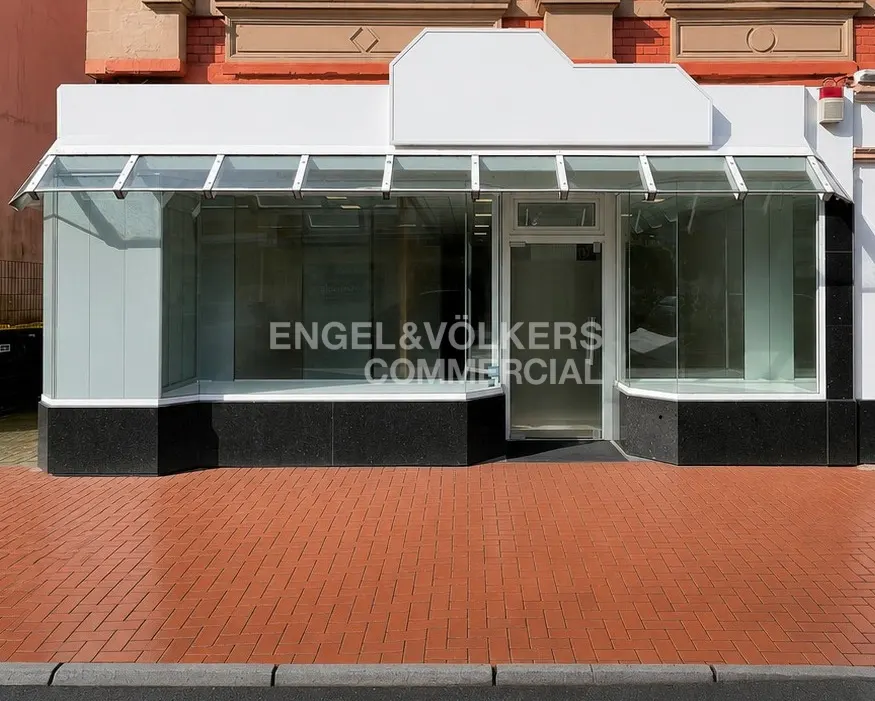 Exterior of Engel & Völkers Commercial storefront with glass windows and a red brick sidewalk.