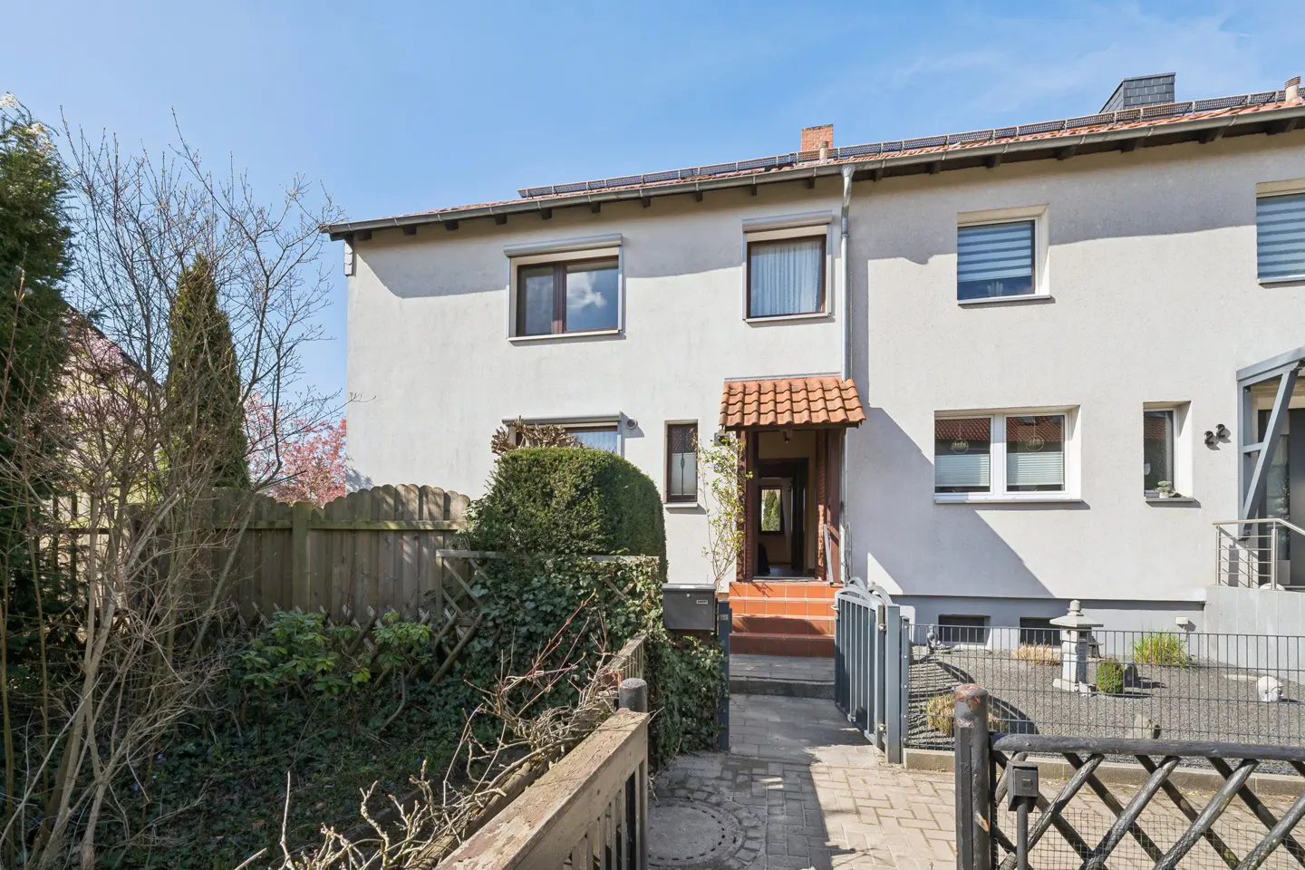 Exterior of a two-story white townhouse with a red tile roof and a small front yard with a wooden fence.