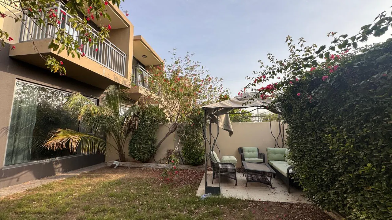 A backyard with a patio set under a canopy, a lawn, and a two-story building with balconies.