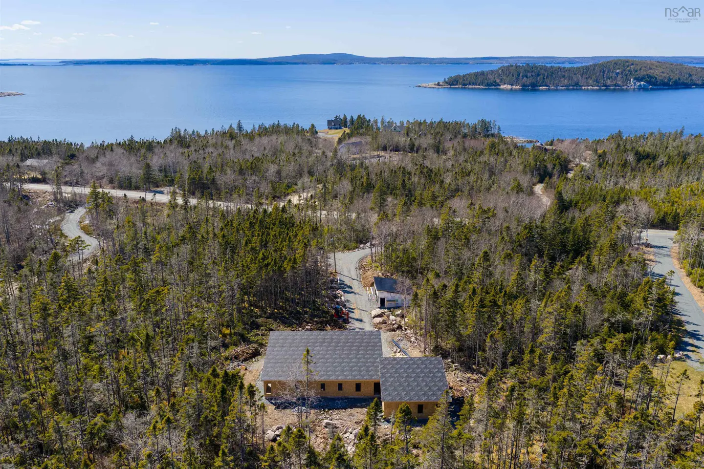 Aerial view of a house with a gray roof surrounded by green trees, with a blue ocean in the background.