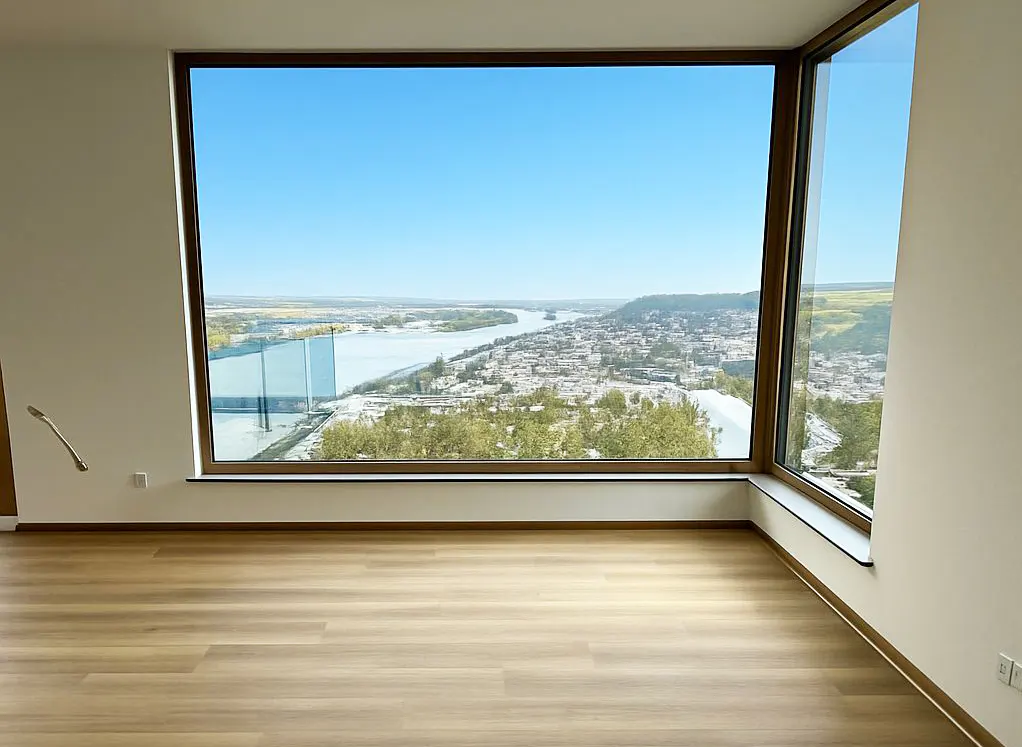 Empty room with wood floors and large windows. Outside is a river, town, and blue sky.