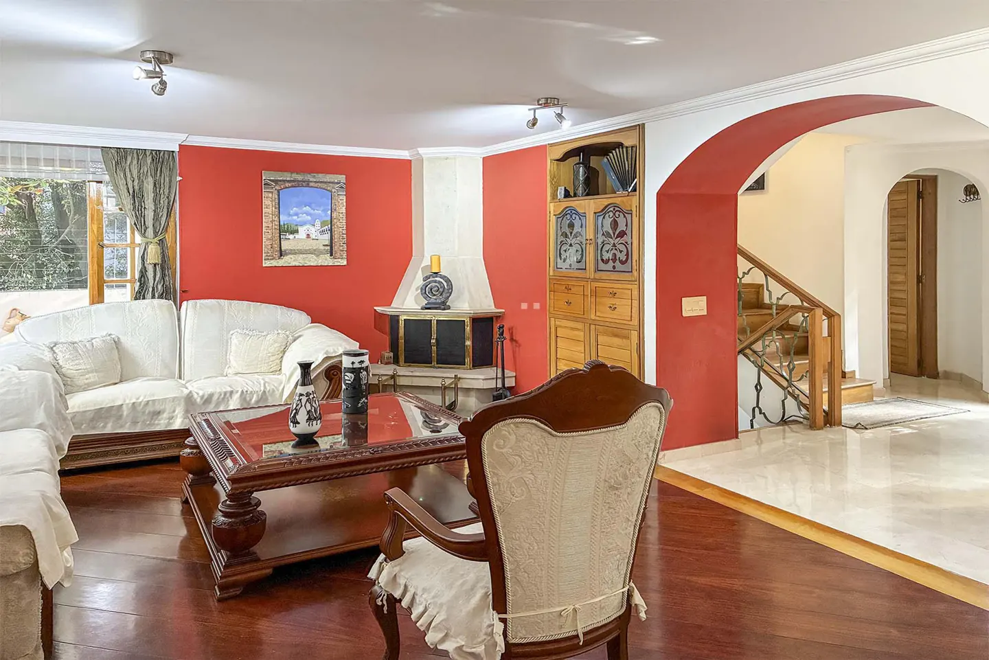 Living room with bright red walls, white sofas, a wooden coffee table, a corner fireplace, and an arched hallway to stairs.