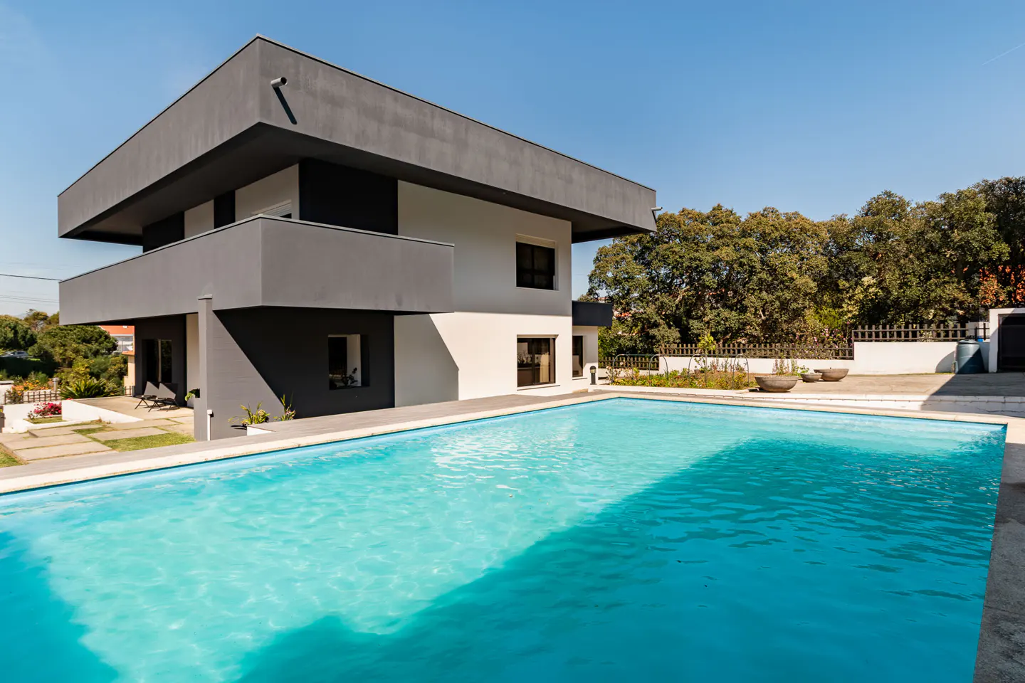 Modern two-story house with a turquoise swimming pool in the foreground on a sunny day.